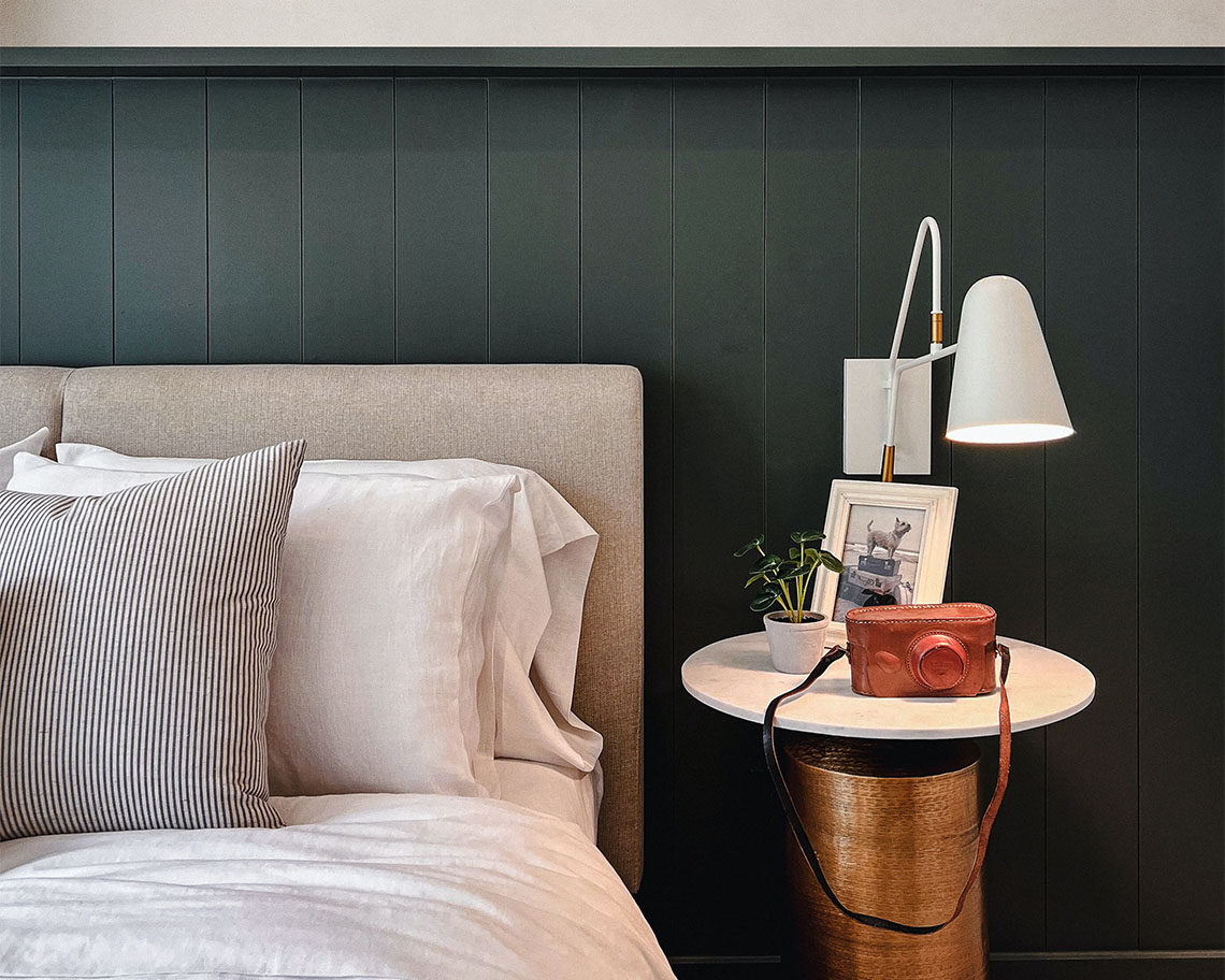 Bed with plush bedding, bedside table with decor, and wall mounted lamp.